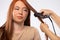 Hairstyle for a redhaired woman using a hair straightener while looking to the side. Beauty service. White background