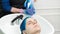 Hairstylist hands squeezes shampoo from tube into head woman with blue hair while washing hair in special sink at beauty