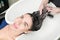 Hairstylist& x27;s hands wash long hair of brunette woman with shampoo in special sink for shampooing