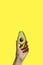 Half an avocado in hand on yellow background