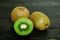 Half bright juicy ripe beautiful kiwi and two whole kiwis on a coarse dark wooden background from boards