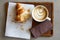 Half eaten croissant with cappuccino on wood tray from above.