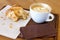 Half eaten croissant with cappuccino on wood tray and table.