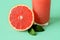 Half of fresh ripe grapefruit at glass of freshly squeezed grapefruit juice with pulp on mint green background. Vegetarian, raw