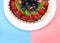 Half a fresh summer fruit pie on plate pink blue backgrounds