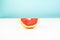 Half of grapefruit on white and blue background. Minimalistic image of slice of citrus at sparse bright environment.