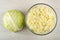 Half head of cabbage, transparent bowl with chopped cabbage on wooden table. Top view