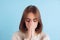 Half-length portrait of young beuatiful girl, student in brown hoodie has a headache isolated on light blue studio