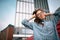 Half length portrait of young woman wearing blue shirt holding hands on the head while standing near office building. Successful