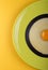 Half of olive color plate with black and white linguini pasta with egg yolk in the middle on yellow background. Top view