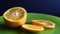 Half an orange and slices on a green glass plate with drops of water, on a table close-up, on a black background. The fruit is