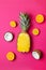 Half pineapple, coconut, lemon and orange on a pink background, vertical photo