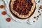 A half of plums pie with dried apricots on dark plate decorated with brown raisins on light table with white cloth