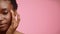 Half-Portrait Of Black Woman Applying Moisturizer On Face, Pink Background