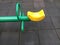 A half of seesaw with black floor background at the playground. Green and yellow seesaw.