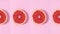 Half sliced grapefruit in a row rotating on pastel pink background. Stop motion flat lay