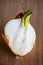 A half of a sprouting bulb or common onion and lying on a wooden cutting board. The layers of the vegetable are visible and also