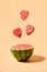 Half of watermelon flying hearts under beige paper background. Vertical composition