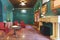 Hall of a vintage-style bar with green walls, a marble fireplace and armchairs upholstered in red fabric, round wooden tables and