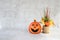 Halloween background with sculpture pumpkin with big smile and small pot autumn`s flower on white grayconcreate or cement wall