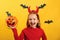 Halloween celebration. Little girl in a devil costume holds a bucket of pumpkin on a yellow background