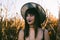 Halloween costume witch girl portrait in a cornfield at sunset. Beautiful serious young woman in witches hat with long black hair