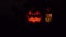 Halloween glowing pumpkins with black background. Orange glow light inside of carved pumpkin heads. Dark smile faces.