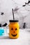 Halloween healthy pumpkin or carrot drink in the glass jar with scary face on a gray background