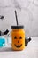 Halloween healthy pumpkin or carrot drink in the glass jar with scary face on a gray background