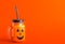 Halloween healthy pumpkin or carrot drink in the glass jar with scary face on a orange background