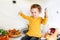 Halloween holiday , child on the kitchen holding spoon and sitting near decorations pumpkin on the table