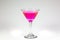 Halloween inspired pink color cocktail in a clear glass sitting on a white table waiting to be enjoyed.