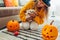 Halloween jack-o-lantern pumpkins. Woman in hat playing with cat wearing ghost clothing on floor decorated with pumpkins