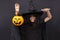 Halloween kid raises his hands up holding jack o lantern and makes faces to scare and get sweets. Child in black