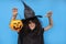 Halloween kid raises his hands up holding jack o lantern and makes faces to scare and get sweets. Child in black