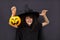 Halloween kid raises his hands up holding jack o lantern and makes faces to scare and get sweets. Child in black