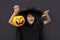 Halloween kid raises his hands up holding jack o lantern and makes faces to scare and get sweets. Child in black