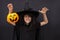 Halloween kid raises his hands up holding jack o lantern and makes faces to scare and get sweets. Child in black