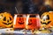 Halloween orange festive drink and pumpkin guards on gray autumn background with sweet corn, fallen leaves and fire lights,