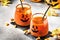 Halloween orange festive drink and pumpkin guards on gray autumn background with sweet corn, fallen leaves and fire lights,
