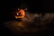 Halloween, orange pumpkin with a scary luminous face on a dark background. Thick gray smoke comes out and spreads across