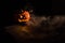 Halloween, orange pumpkin with a scary luminous face on a dark background. Thick gray smoke comes out and spreads across the black