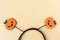 Halloween party accessory, rim with two shiny pumpkins with cute creepy faces. Pastel yellow background, place for text.