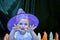 Halloween portrait of little girl wearing purple witch hat scaring the audience against black backgorund. Kid`s custom