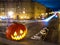 Halloween pumpkin on the background of the night city. Buildings and streaks of light from cars passing along the road