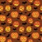 Halloween seamless pattern with orange pumpkins carved faces and black bats on brown background