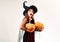 Halloween Surprised woman witch. Woman posing with Pumpkin. Beautiful young surprised woman in witches hat and costume