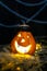 Halloween symbol - glowing Jack o`Lantern pumpkin head with lamp in a pointed black hat in the hay on the background of cobweb