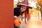 Halloween trick or treat.Happy girl wearing a witch`s hat, with a pumpkin handbag, peeps out from behind a Orange wall. Funny kid