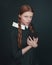 Halloween vampire woman looks directly into the camera holding book. Female portrait in vintage style on dark background.